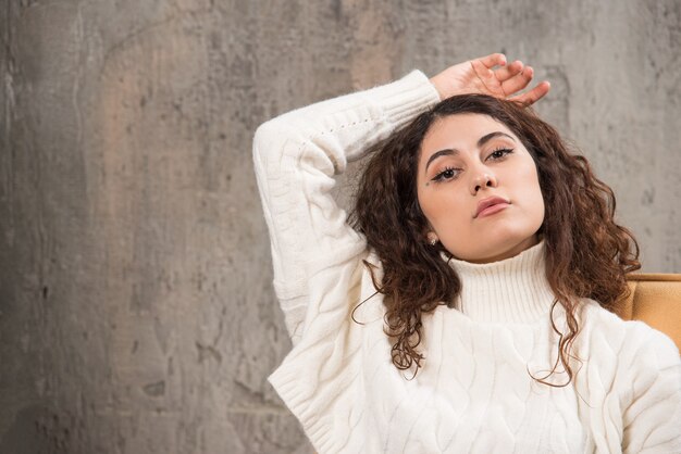 Foto de atractiva dama sentada en una cómoda silla y posando