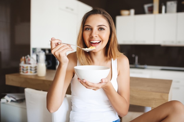 Foto de atractiva jovencita comiendo copos de maíz con leche en la cocina