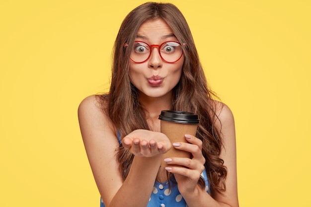 Foto de atractiva mujer europea con cabello largo y oscuro, lleva gafas transparentes con montura roja