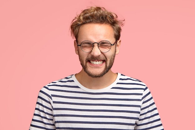 Foto de atractivo hombre alegre se ríe positivamente de la cámara, mantiene los ojos cerrados