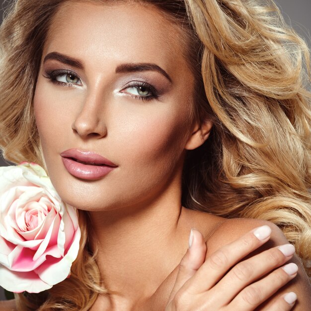 Foto de una bella mujer rubia con flor. Primer atractivo rostro sensual de mujer blanca con pelo rizado. Maquillaje de ojos ahumados.