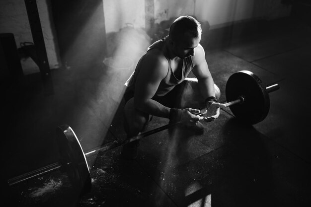 Foto en blanco y negro de un hombre musculoso usando tiza deportiva en las manos mientras levanta pesas en un gimnasio