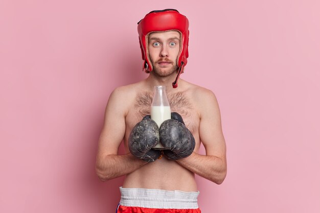 Foto de un boxeador decidido que tiene como objetivo ganar el juego. Prepárese para la pelea, usa guantes de boxeo y un casco protector bebe leche como fuente de calcio.