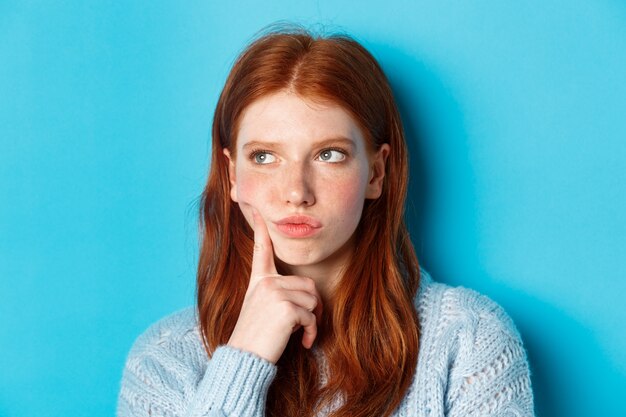 Foto de cabeza de una adolescente con problemas pensando, mirando molesto y frunciendo el ceño, de pie contra el fondo azul.