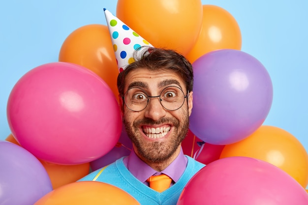 Foto de cabeza de chico guapo alegre rodeado de globos de fiesta posando