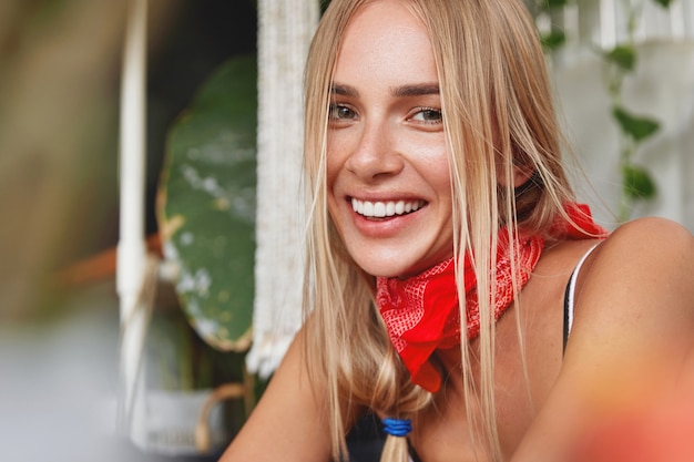 Foto de cabeza de mujer rubia atractiva complacida con expresión positiva y amplia sonrisa