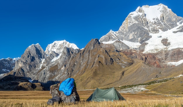 Foto de una carpa verde cerca de una roca en un campo rodeado de montañas cubiertas de nieve