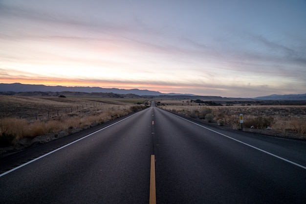 Foto de una carretera rodeada de campos de hierba seca bajo un cielo durante la puesta de sol