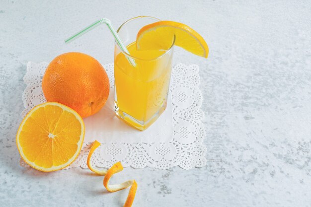 Foto de cerca de la mitad de la naranja cortada o entera con un vaso de jugo en la pared gris.