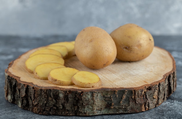 Foto de cerca de patatas en rodajas y enteras sobre tabla de madera.