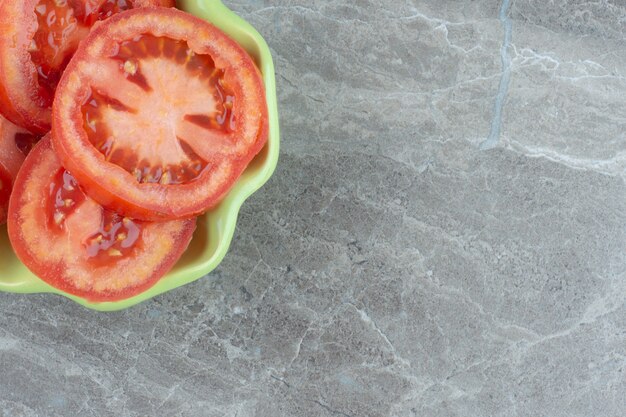 Foto de cerca de tomate rojo en rodajas en un tazón verde.