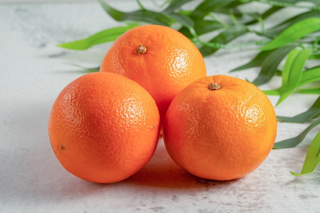 Foto de cerca de tres mandarinas clementinas frescas sobre superficie gris.