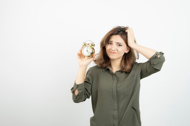 Foto de una chica matutina sosteniendo un despertador sobre una pared blanca. foto de alta calidad