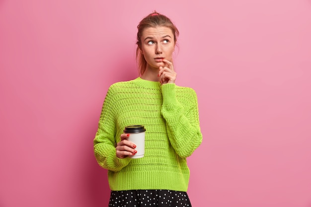 Foto de una chica milenaria pensativa centrada en algún lugar a un lado sostiene un café para llevar toma un descanso del trabajo