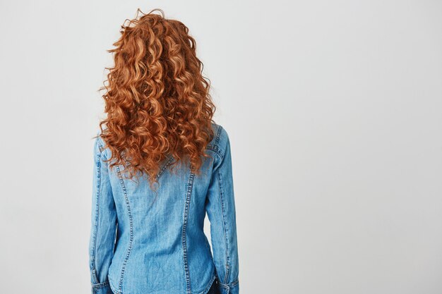 Foto de chica con el pelo rizado rojo de pie de nuevo a la cámara. Copia espacio