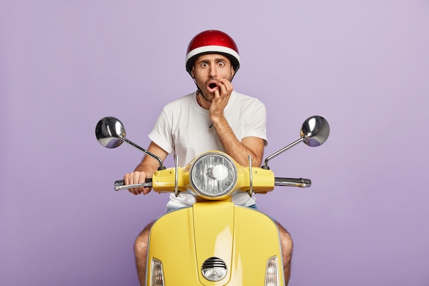 Foto de chico sorprendido con casco conduciendo scooter amarillo