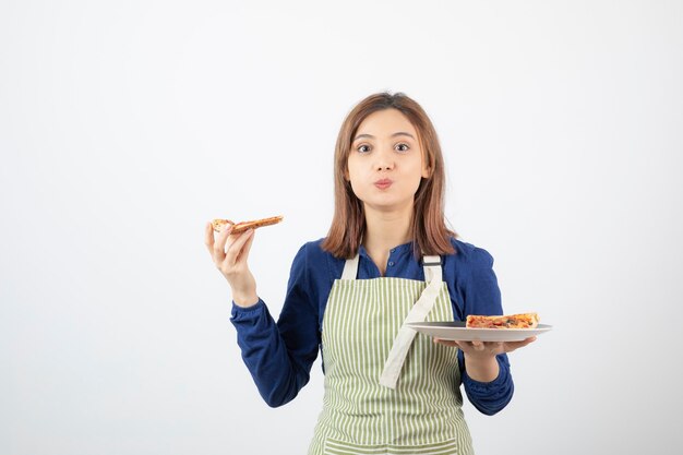 Foto de cocinera en delantal sosteniendo pizza y mirando a la cámara