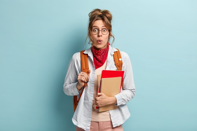 Foto de colegiala sorprendida sostiene blocs de notas, listo para la escuela y estudiar, lleva mochila