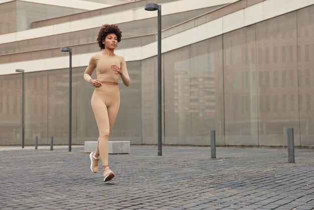 Una foto completa de una joven delgada y activa vestida con ropa deportiva y zapatillas deportivas corre rápido al aire libre tiene un entrenamiento matutino regular enfocado en la distancia La corredora atlética se prepara para el maratón