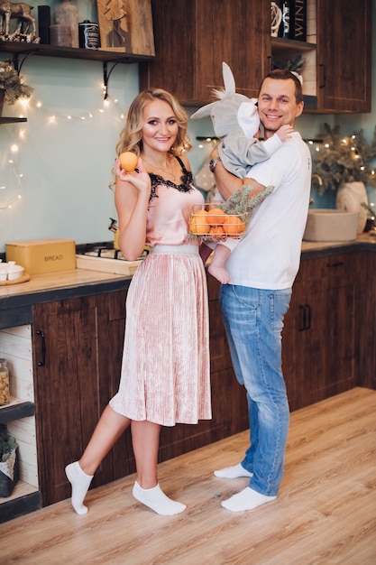 Foto de concepto de Navidad de la pequeña familia alegre de marido, mujer y bebé posando en cocina bien amueblada. Concepto de vacaciones