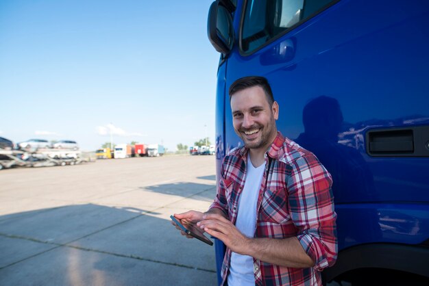 Foto de conductor de camión profesional de pie junto a su camión con tableta y configurando la navegación GPS para el próximo viaje