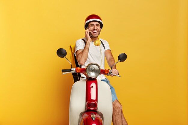 Foto de conductor masculino guapo alegre en scooter con casco rojo