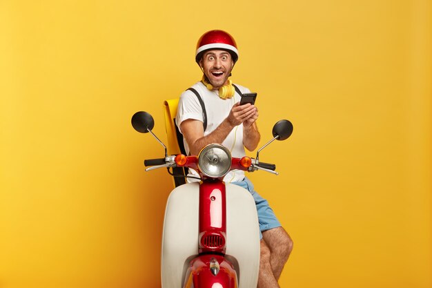 Foto de conductor masculino guapo lleno de alegría en scooter con casco rojo