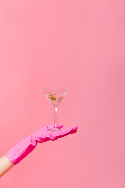 Foto de copa de martini con oliva en mano sobre pared rosa