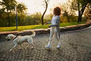 Foto gratuita foto de cuerpo entero de bastante saludable jovencita caminando por la mañana en el parque con perro