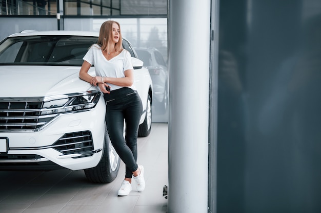 Foto gratuita foto de cuerpo entero. chica y coche moderno en el salón. durante el día en interiores. comprar vehículo nuevo