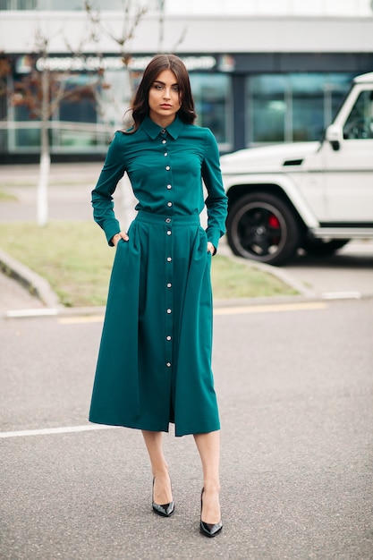 Foto de cuerpo entero de hermosa dama en vestido verde de pie al aire libre mientras posa en la cámara. Concepto de estilo y moda