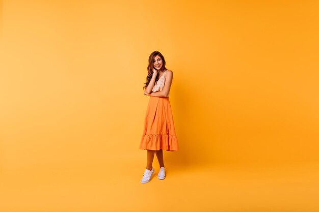 Foto de cuerpo entero de mujer atractiva en falda naranja larga Encantadora modelo femenina caucásica en atuendo de verano pasando tiempo en el estudio