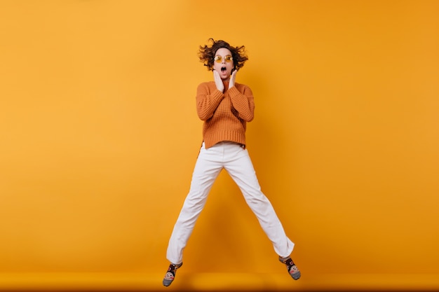 Foto de cuerpo entero de una mujer joven asombrada en pantalones blancos bailando