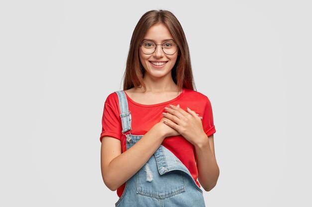 La foto de una dama amigable y complacida mantiene las manos en el pecho o el corazón, siendo movida por palabras positivas