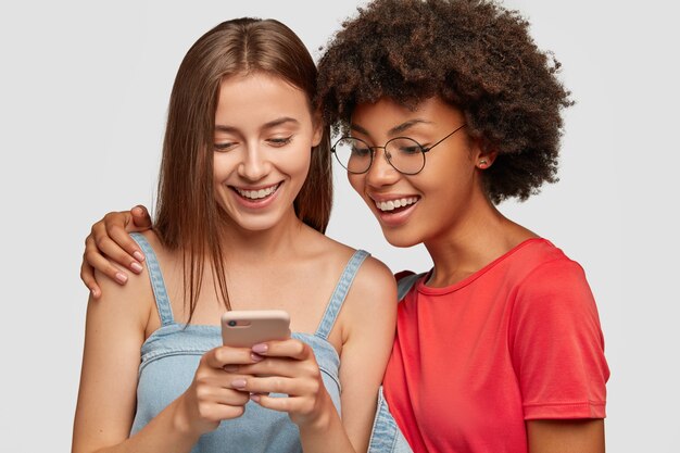 Foto de dos bonitas hermanas multiétnicas que reservan juntas en una página web a través de un teléfono celular