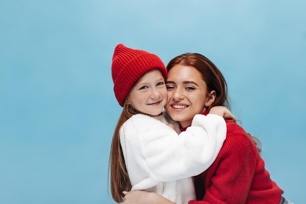 Foto de dos hermanas bonitas con ropa moderna Niña vestida de blanco abraza a una dama sonriente con el pelo moreno en un fondo aislado