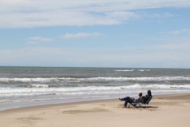 Foto de dos personas sentadas en las sillas en la playa mirando las olas del mar y relajarse