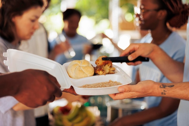 Foto enfocada en un hombre caucásico sirviendo pan, pollo y frijoles horneados a una persona afroamericana pobre y hambrienta en una campaña de comida sin fines de lucro.