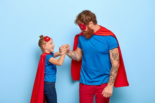 Foto del equipo familiar encantado de superhéroes, la pequeña hija de jengibre y el padre mantienen las manos juntas