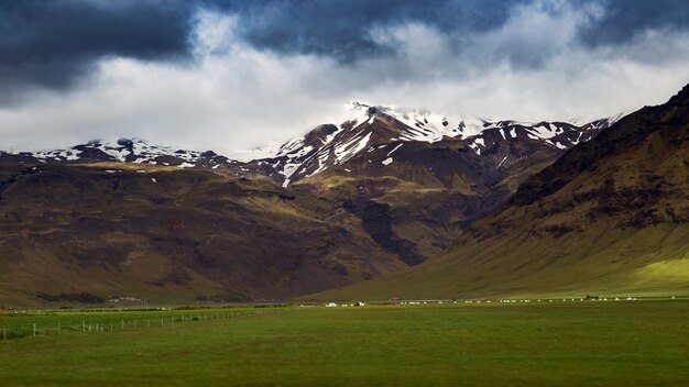 Foto escénica de colinas cubiertas de nieve bajo el cielo nublado azul en frente de un campo