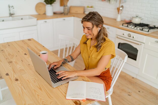 Foto de estilo de vida interior de ama de casa feliz buscando algunos recibos y bebiendo café en una cocina moderna y ligera