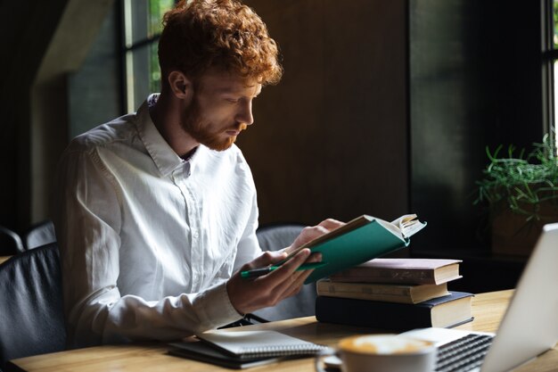 Foto de estudiante barbudo pelirrojo concentrado, preparándose para el examen universitario en un café