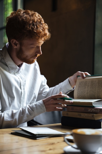 Foto de estudiante barbudo pelirrojo serio, preparándose para el examen en un café