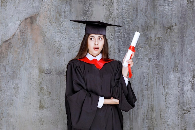 Foto de una estudiante con bata posando con certificado de graduación. foto de alta calidad