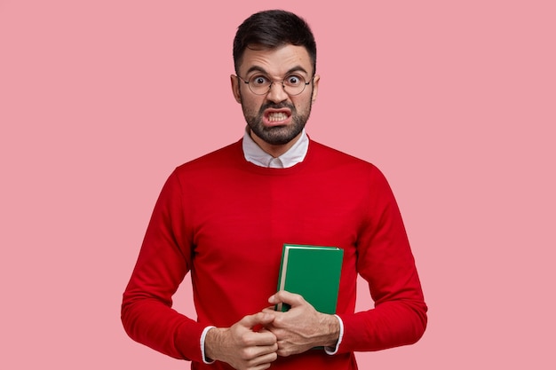 Foto de estudiante enojado e irritado que mira con disgusto y enojo, aprieta los dientes, mira fijamente, usa anteojos redondos