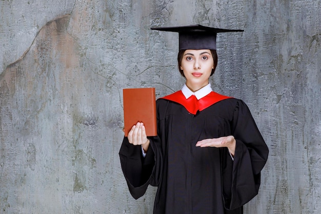 Foto de estudiante graduada inteligente mostrando su libro sobre la pared. foto de alta calidad