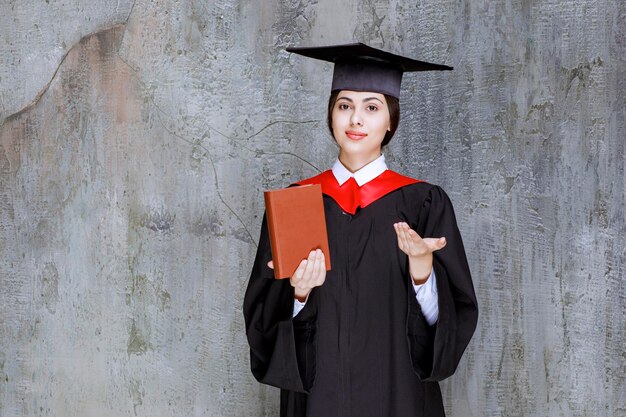 Foto de estudiante de posgrado inteligente mostrando su libro de diploma sobre la pared. foto de alta calidad