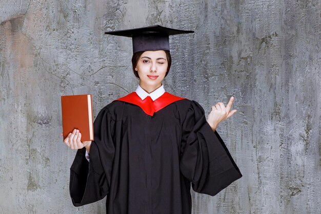 Foto de estudiante de posgrado inteligente mostrando su libro de diploma sobre la pared. foto de alta calidad