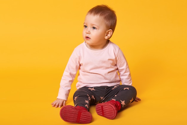 Foto gratuita foto de estudio de adorable pequeña niña sentada en el piso