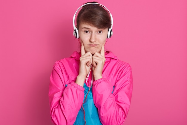 Foto de estudio de alegre joven caucásica deportiva en ropa deportiva con auriculares blancos en la cabeza, escuchando música, parece molesto